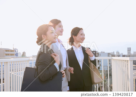 三位年輕的職業女性沐浴著晨光走向工作地點;一位身著西裝的新員工在求職和通勤途中,以積極的態度向前走去。 三位年輕的職業女性沐浴著晨光走向工作地點;一位身著西裝的新員工在求職和通勤途中,以積極的態度向前走去。 139420817