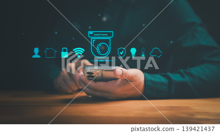 Smart home automation system with security camera and mobile control. Hand holding smartphone for IoT house protection, monitoring, and remote wireless technology. Smart home automation system with security camera and mobile control. Hand holding smartphone for IoT house protection, monitoring, and remote wireless technology. 139421437