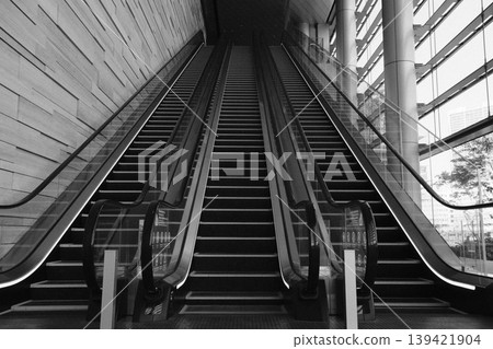 以單色描繪的城市建築之美:建築物內部排列的自動扶梯和光線充足的中庭空間。 以單色描繪的城市建築之美:建築物內部排列的自動扶梯和光線充足的中庭空間。 139421904