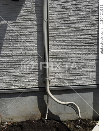 Exposed air conditioner piping and drain hose on the exterior wall of a house Exposed air conditioner piping and drain hose on the exterior wall of a house 139421951