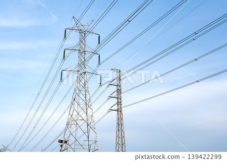 High-voltage electricity transmission towers and power lines against a bright blue sky. Industrial infrastructure for electric energy distribution and power supply systems in clear outdoor setting. High-voltage electricity transmission towers and power lines against a bright blue sky. Industrial infrastructure for electric energy distribution and power supply systems in clear outdoor setting. 139422299