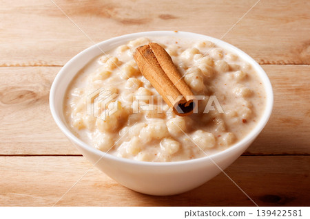 Creamy white corn porridge with cinnamon sticks in a white bowl on a wooden table 139422581