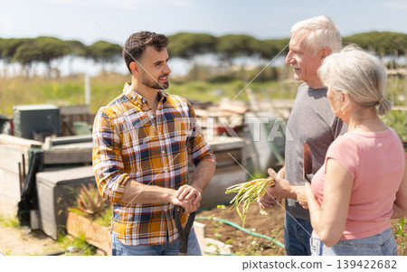 Elderly couple and young man talking together on farm field 139422682