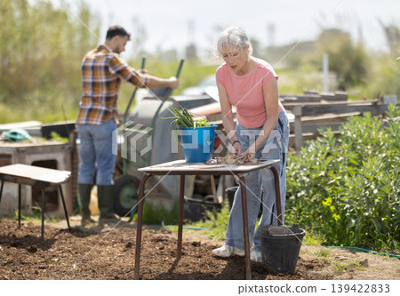 Mature woman works in the garden outdoors - preparing various tools for caring for plants Mature woman works in the garden outdoors - preparing various tools for caring for plants 139422833