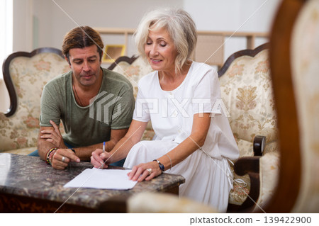 Helpful man helping elderly woman to sign documents Helpful man helping elderly woman to sign documents 139422900