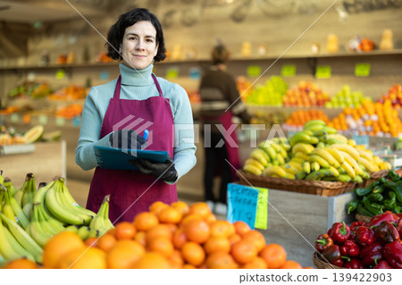 Woman store employee with folder of documents takes inventory in vegetable store Woman store employee with folder of documents takes inventory in vegetable store 139422903