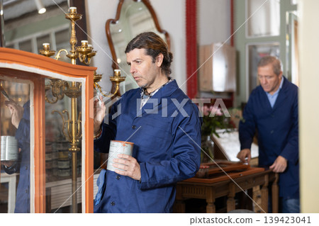 Male furniture maker diligently working on vintage glass cabinet in workshop Male furniture maker diligently working on vintage glass cabinet in workshop 139423041