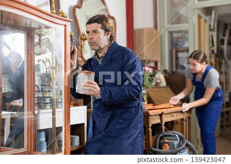 Male furniture workshop worker repainting vintage glass cabinet Male furniture workshop worker repainting vintage glass cabinet 139423047