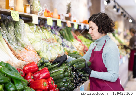 Woman shop seller puts zucchini goods on display case Woman shop seller puts zucchini goods on display case 139423160