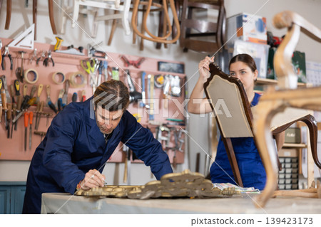 Male and female carpenters working on restoring vintage mirror and chair in workshop Male and female carpenters working on restoring vintage mirror and chair in workshop 139423173