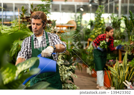 Portrait of a gardener watering flowers in a greenhouse Portrait of a gardener watering flowers in a greenhouse 139423302