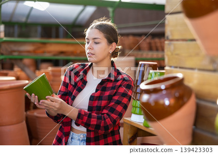 Young woman chooses flower pots for indoor plants Young woman chooses flower pots for indoor plants 139423303