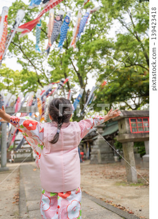 A child in a kimono looks up at a carp streamer. A child in a kimono looks up at a carp streamer. 139423418