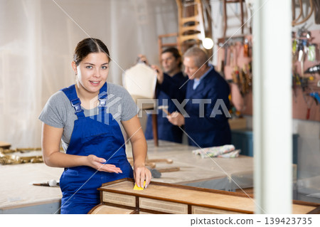 Skilled female furniture repair specialist in uniform restoring Victorian dresser during workday in workshop Skilled female furniture repair specialist in uniform restoring Victorian dresser during workday in workshop 139423735