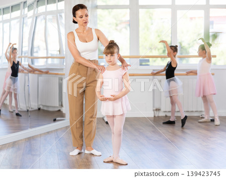 Ballet lesson for little girls - choreography teacher shows little ballerinas how to get into different poses correctly in sturio 139423745