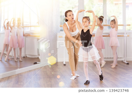 In studio, mentor corrects girls arm and leg, teaches correct dynamics and execution of movements 139423746
