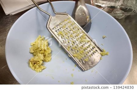 Freshly Grated Ginger Root in a Blue Bowl with a Stainless Steel Grater Freshly Grated Ginger Root in a Blue Bowl with a Stainless Steel Grater 139424830