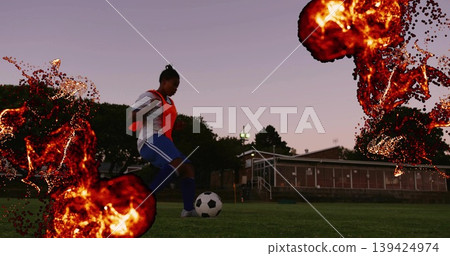 Dribbling soccer player wearing orange bib on grass field under field lights, with ball, copy space 139424974