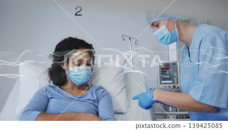 Pointing nurse explaining infusion pump next to patient wearing surgical mask in hospital room 139425085