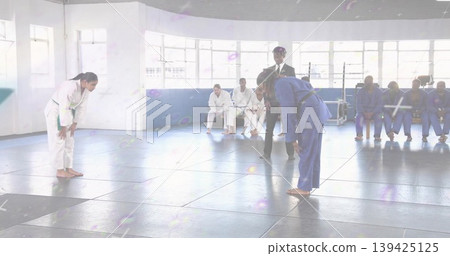 Bowing competitors wearing white and blue gis with green and black belts at dojo, padded mats 139425125