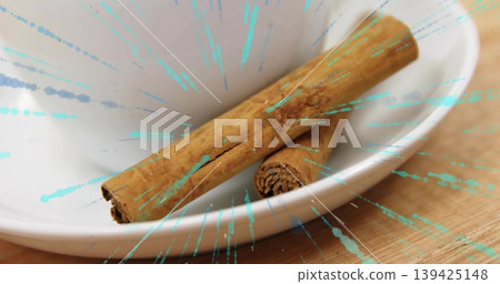 Featuring white ceramic bowl holding brown cinnamon sticks on wooden countertop, with teal splashes Featuring white ceramic bowl holding brown cinnamon sticks on wooden countertop, with teal splashes 139425148