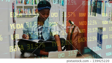 Writing student referencing laptop, notebook and pen in library aisle, with financial data overlay Writing student referencing laptop, notebook and pen in library aisle, with financial data overlay 139425220