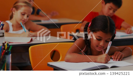 Writing braided-hair girl using pen on notebook at classroom desks, with colored-pencil container Writing braided-hair girl using pen on notebook at classroom desks, with colored-pencil container 139425221