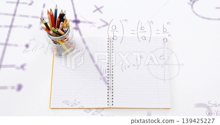 Showing open spiral notebook on white desk, with glass jar holding colored pencils, math overlays 139425227