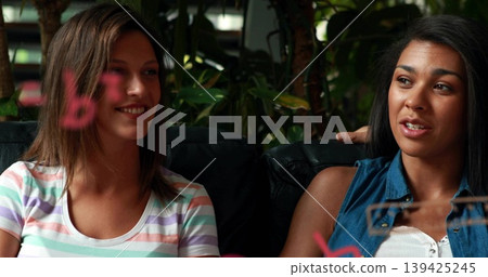 Two women wearing striped tee and denim chatting in lounge, with couch, plants and marker board Two women wearing striped tee and denim chatting in lounge, with couch, plants and marker board 139425245