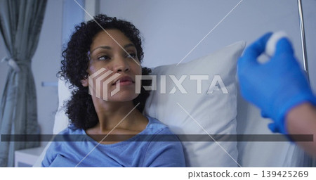 Patient wearing gown lying on bed receiving injection in ward, with syringe, pillows, IV stand 139425269