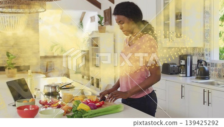 Chopping woman wearing pink tee and jeans preparing bell peppers on cutting board in home kitchen 139425292