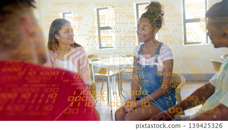 Collaborating group with woman wearing overalls sharing code in classroom, notebook binary overlay Collaborating group with woman wearing overalls sharing code in classroom, notebook binary overlay 139425326