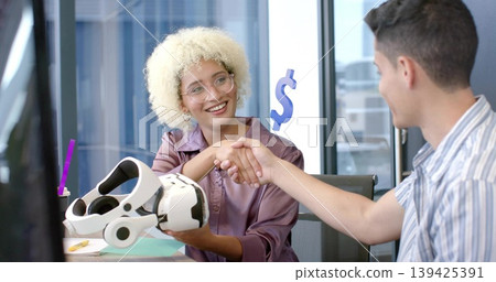 Shaking hands female tech pro and business associate at office desk, with virtual reality headset Shaking hands female tech pro and business associate at office desk, with virtual reality headset 139425391