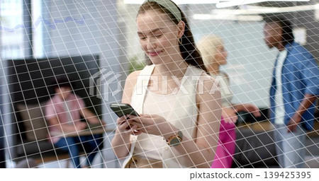 Office professional woman holding smartphone while standing in office lounge, with seating benches Office professional woman holding smartphone while standing in office lounge, with seating benches 139425395