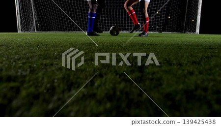 Contesting ball between two male players on nighttime soccer field, with turf, goal net, cleats Contesting ball between two male players on nighttime soccer field, with turf, goal net, cleats 139425438