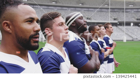 Standing rugby players placing hand on chest on pitch wearing jerseys, shorts, headband by goalpost Standing rugby players placing hand on chest on pitch wearing jerseys, shorts, headband by goalpost 139425441