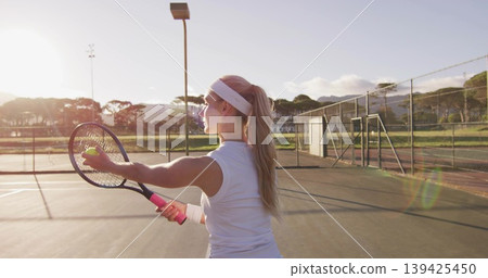 Holding racket and ball, woman tennis player preparing serve on hard court, with net, fence Holding racket and ball, woman tennis player preparing serve on hard court, with net, fence 139425450