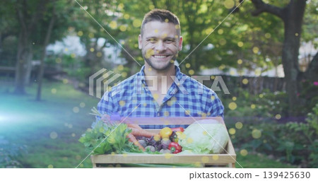 Smiling mid adult man holding wooden crate of fresh vegetables in backyard garden, dappled sunlight 139425630