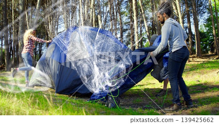 Three friends hoisting blue tent frame and pulling rainfly in sunlit pine forest, green guy lines Three friends hoisting blue tent frame and pulling rainfly in sunlit pine forest, green guy lines 139425662
