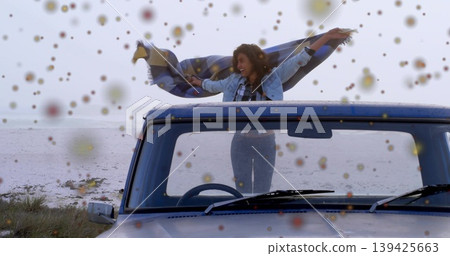 Lifting checkered blanket, woman wearing denim outfit in pickup truck at shore, water, hills 139425663