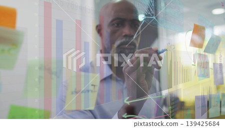 African American man drawing charts on glass board in office, with marker, sticky notes African American man drawing charts on glass board in office, with marker, sticky notes 139425684
