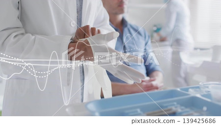 Female doctor in white coat putting latex glove at exam room table, with blue instrument tray Female doctor in white coat putting latex glove at exam room table, with blue instrument tray 139425686