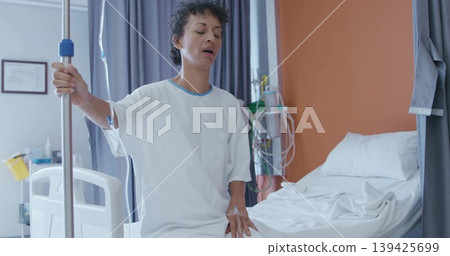 Patient holding IV pole and resting hand on leg in hospital room, with infusion pump 139425699
