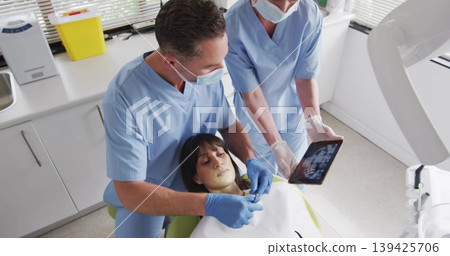 Reclining patient in dental chair wearing bib getting exam and tablet with X-ray in treatment room Reclining patient in dental chair wearing bib getting exam and tablet with X-ray in treatment room 139425706