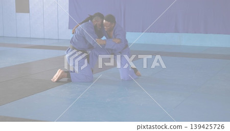 Grappling adult practitioners wearing blue gis on interlocking mats in dojo, with curtain backdrop Grappling adult practitioners wearing blue gis on interlocking mats in dojo, with curtain backdrop 139425726