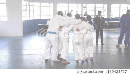 Cheering martial arts team gathering in training hall, lifting gold trophy and wearing white gis Cheering martial arts team gathering in training hall, lifting gold trophy and wearing white gis 139425727