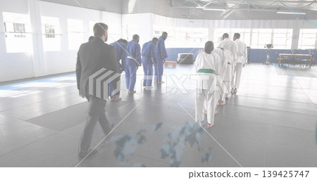 Walking instructor in dark suit approaching bowing martial artists on dojo mats, with gis and belts Walking instructor in dark suit approaching bowing martial artists on dojo mats, with gis and belts 139425747