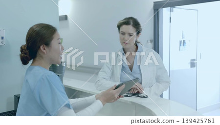 Reviewing nurse in scrubs and doctor in lab coat at curved clinic counter, with tablet, stethoscope Reviewing nurse in scrubs and doctor in lab coat at curved clinic counter, with tablet, stethoscope 139425761