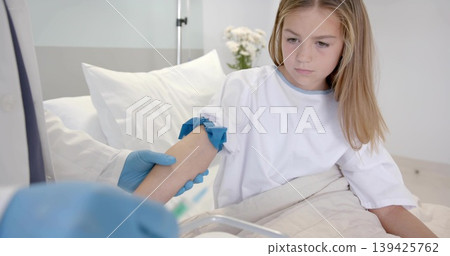 Nurse wearing blue gloves applying tourniquet on girl wearing medical gown, on hospital bed Nurse wearing blue gloves applying tourniquet on girl wearing medical gown, on hospital bed 139425762