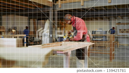 Sanding carpenter wearing red shirt and goggles smoothing plank in workshop, with portable sander Sanding carpenter wearing red shirt and goggles smoothing plank in workshop, with portable sander 139425781